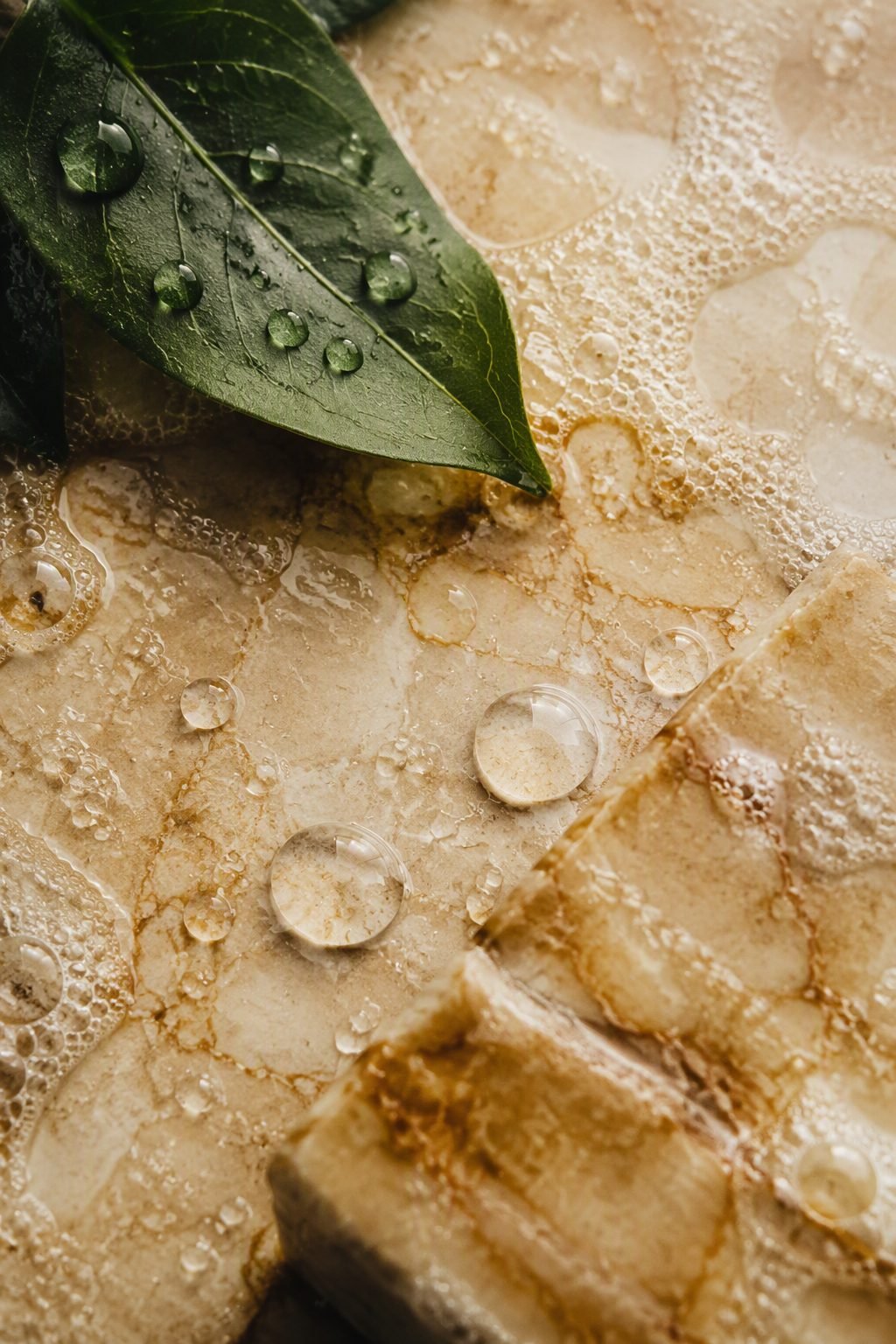 Gotas de agua y espuma fina sobre piedra cálida con una hoja verde.